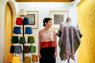 A photograph of Gabriela Martínez Ortiz in her studio in Mexico, stood next to large cotton reels on a stand