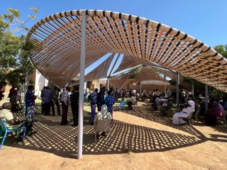 People gather in the sunshine under the semi-circular community tent built by Safeguarding Sudan's Living Heritage in the space outside Albarkal Museum in the Northern State.